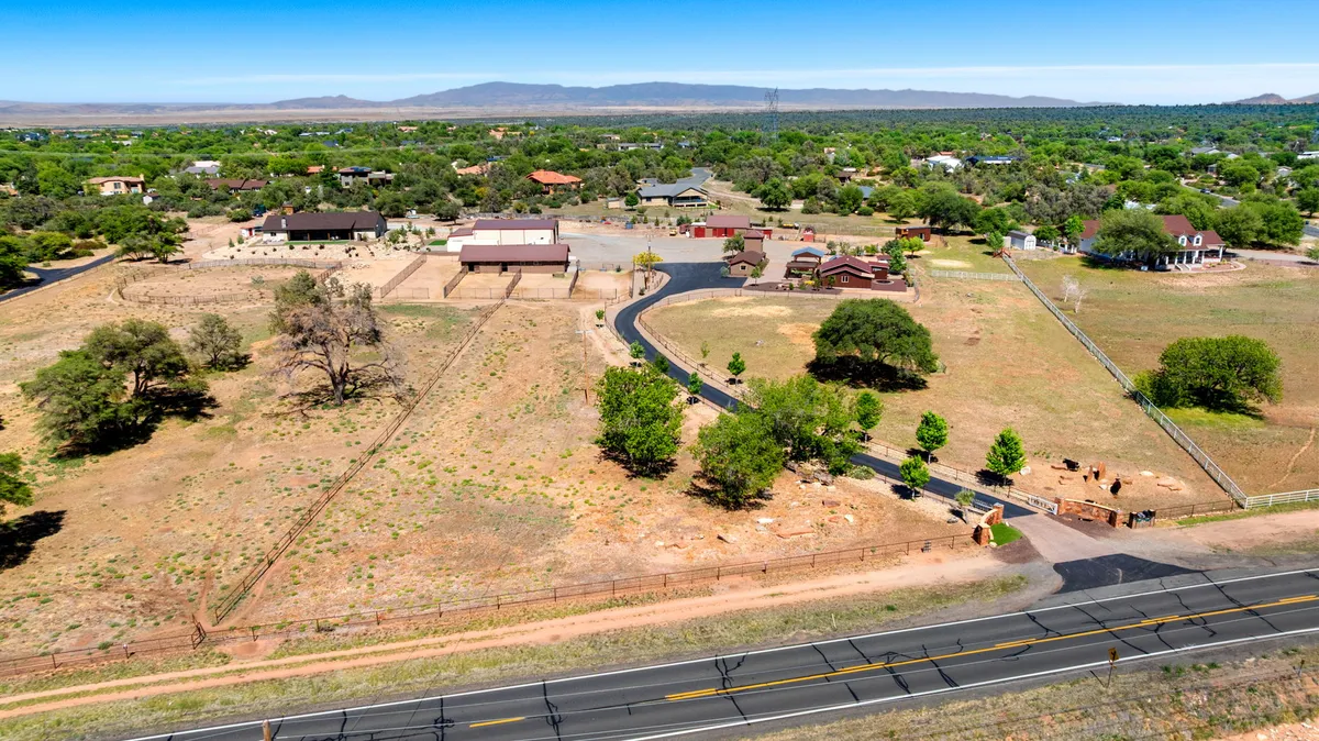 A sweeping view of the property reveals fenced pastures, lush greenery, and a winding road leading to the ranch, with mountains forming a scenic backdrop. The expansive layout suggests plenty of space for animal habitats, exploration, and family adventures.