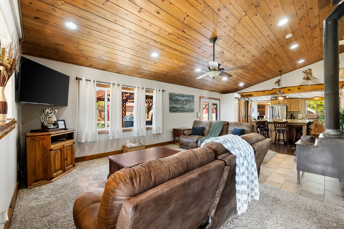 This interior shot features a cozy living room with wooden ceilings, plush sofas arranged for conversation or movie nights, a large television, and an adjacent dining area. The space is bright, inviting, and clearly designed for both relaxing and entertaining.