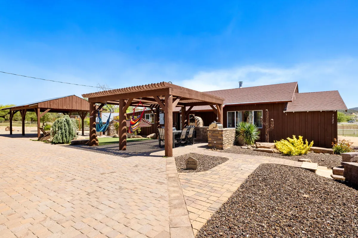 The image showcases a beautifully landscaped garden with inviting pergola structures, cozy hammocks gently swaying, an outdoor seating area perfect for gatherings, and hints of a fire pit. The sun is setting, casting a warm, tranquil glow over the scene, evoking relaxation and togetherness.